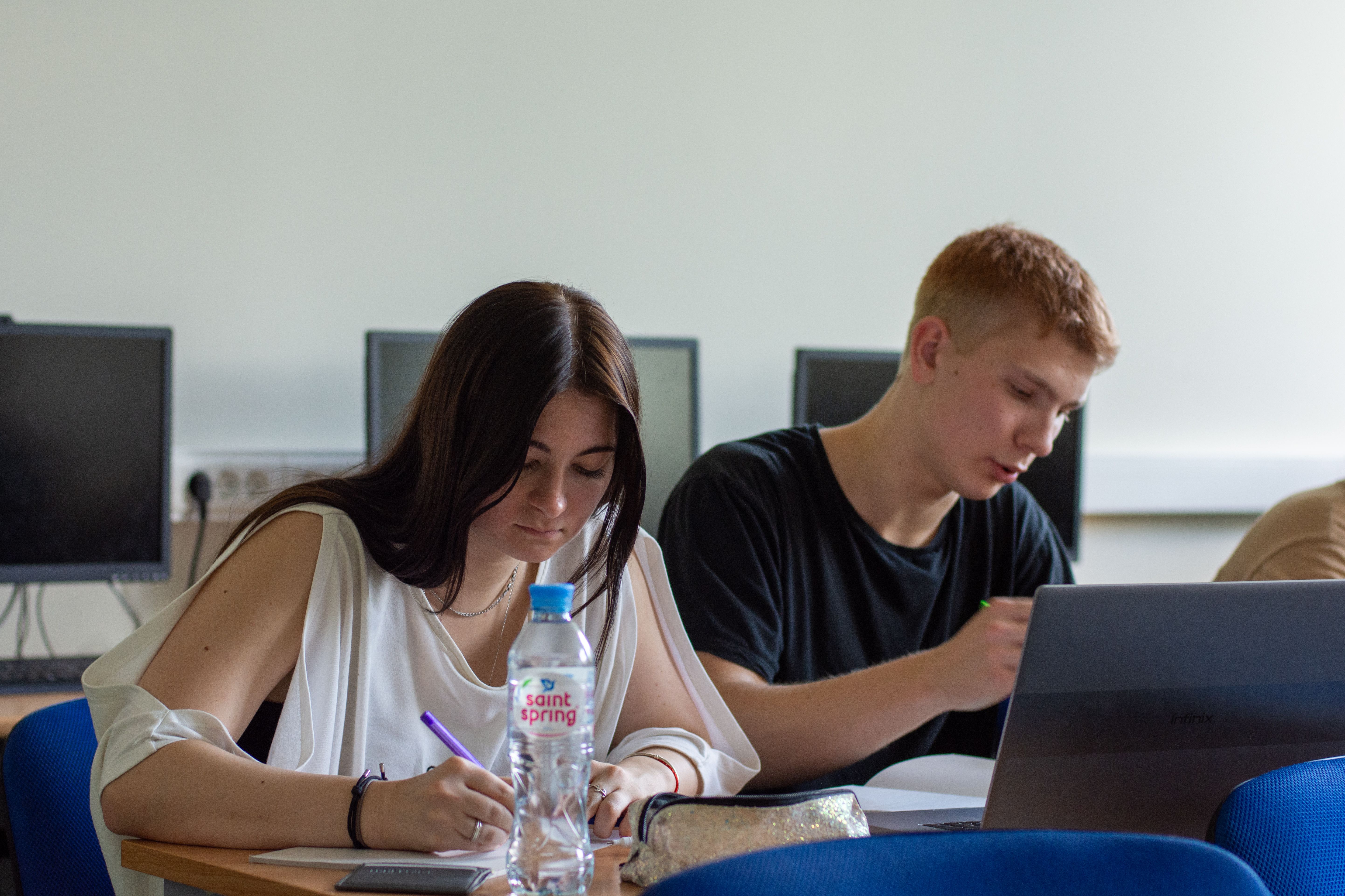 Two students working on a laptop in a computer lab, learning about academic integrity and AI tools